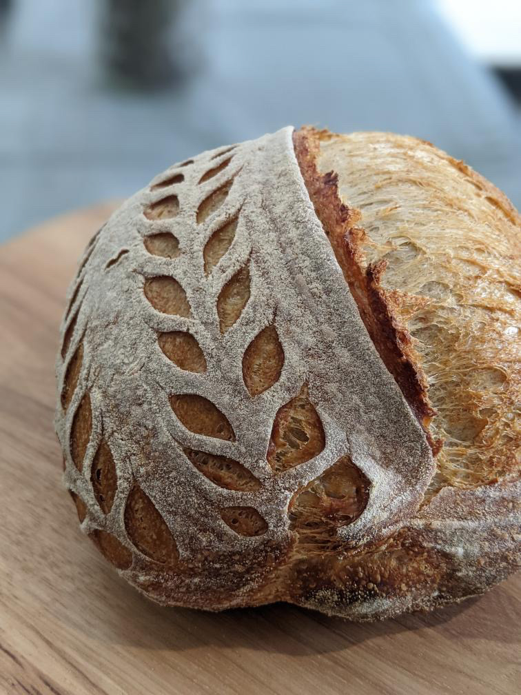 Photo of a loaf of sourdough bread with an intricate leaf pattern on top