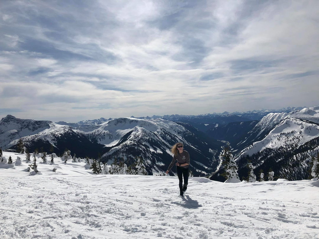 Photo of a person climbing a snowy mountaintop, with more mountains stretching out as far as the eye can see