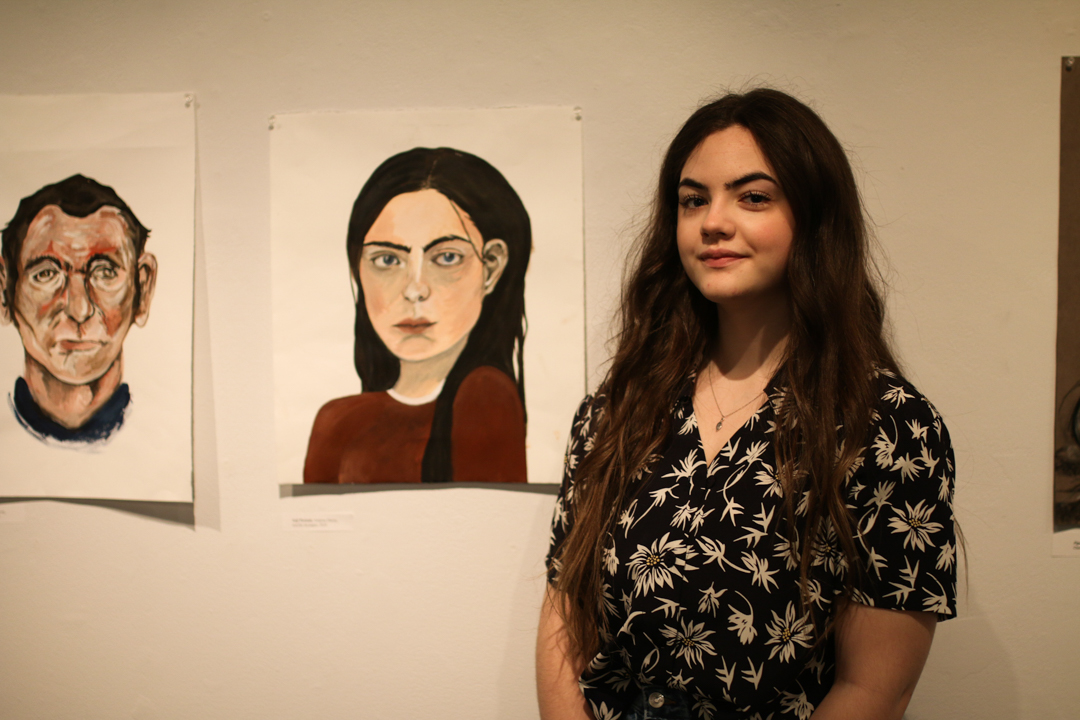 Photo of Aislynn Davey next to several pieces of their art