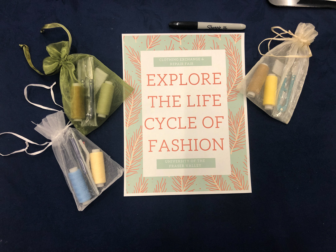 Photo of a sign reading "explore the life cycle of fashion" with small bags containing needles and threads arranged around it