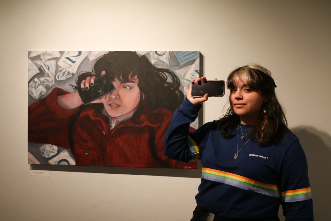 Photo of Noelani Leon next to a self-portrait; Noelani is mirroring the portrait's pose by holding a phone up over her eye.