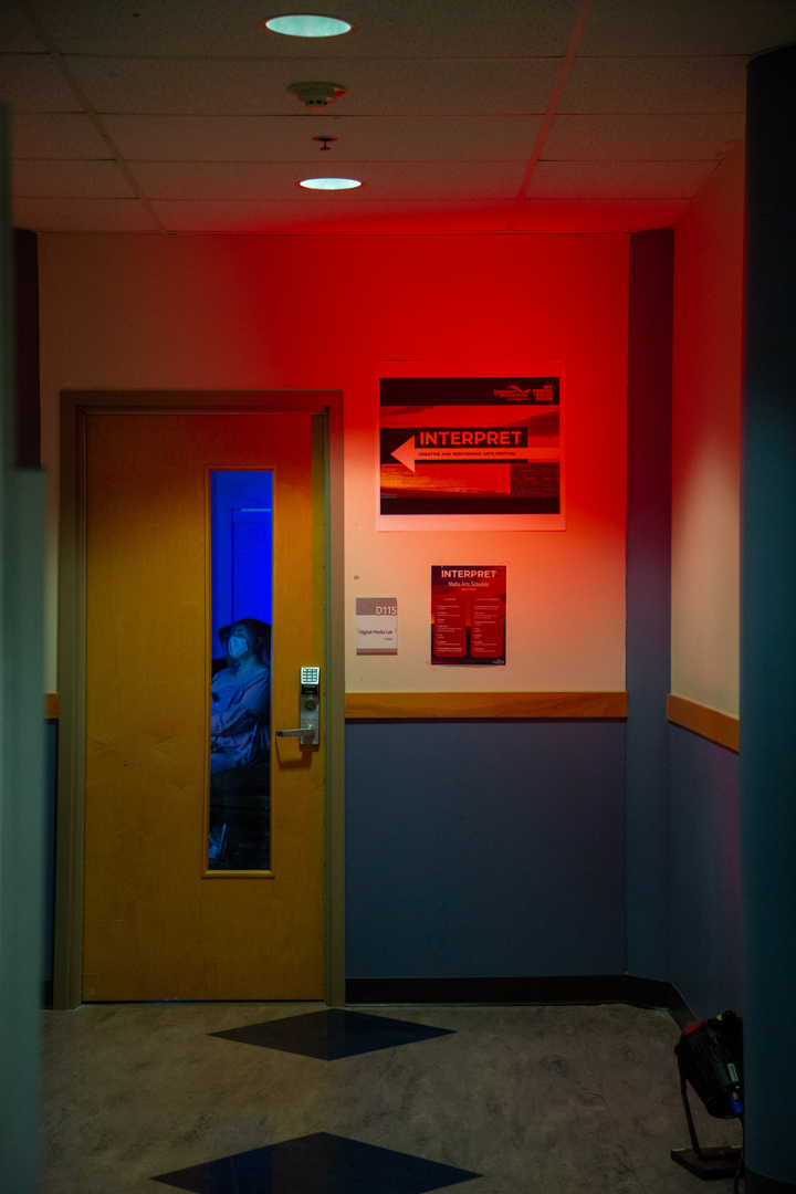 Photo taken through a glass window in a door. Through the window is a strong blue light, and a person looking at something out of the camera's view. A sign next to the door points towards it, and reads "Interpret"