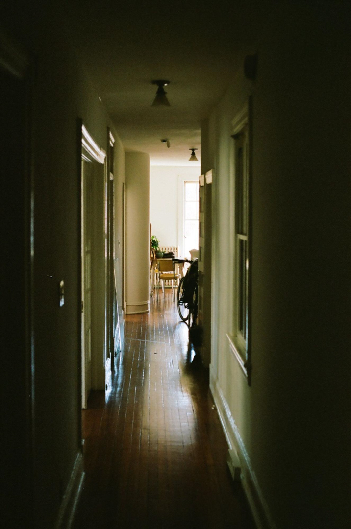 Photo of a hallway in home, dark near the camera and emerging into light at the far end of the hallway