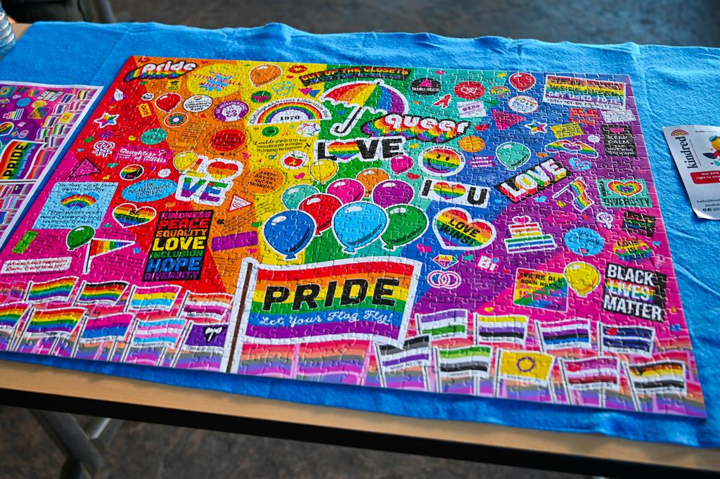This image shows a close-up of a puzzle on a table. The puzzle is composed of colorful text and shapes, with the majority of the colors being blue. In the background, there is also an open book that has been placed next to it.