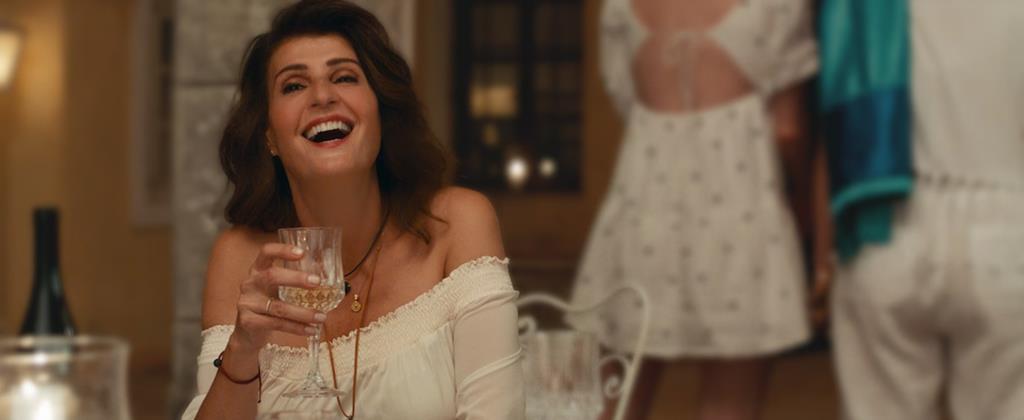 A woman in a restaurant wearing a white dress holding a glass of wine laughinng