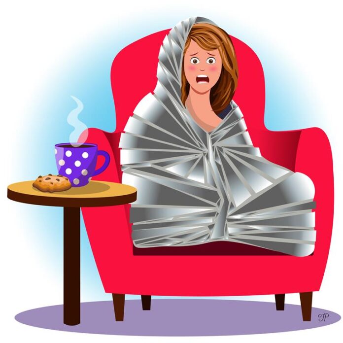 A girl wrapped in a foil blanket sits in an armchair, looking shocked. Tea and a cookie are on the table next to her.