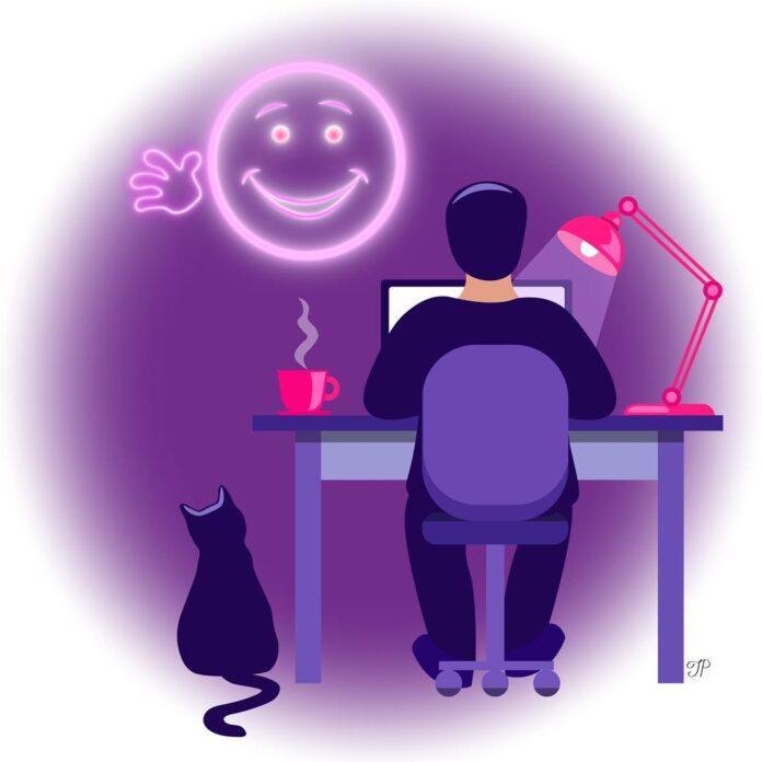 A boy sits at the computer desk at home at night with a big smiley neon light shining at him.