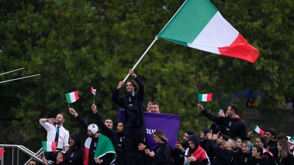 Gianmarco Tamberi waves an Italian flag as the Italian team parades along the Seine river in Paris, France, during the opening ceremony of the 2024 Summer Olympics, Friday, July 26, 2024