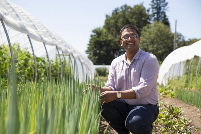 Photo of Saeed Rahman crouching down next to a garden and greenhouse