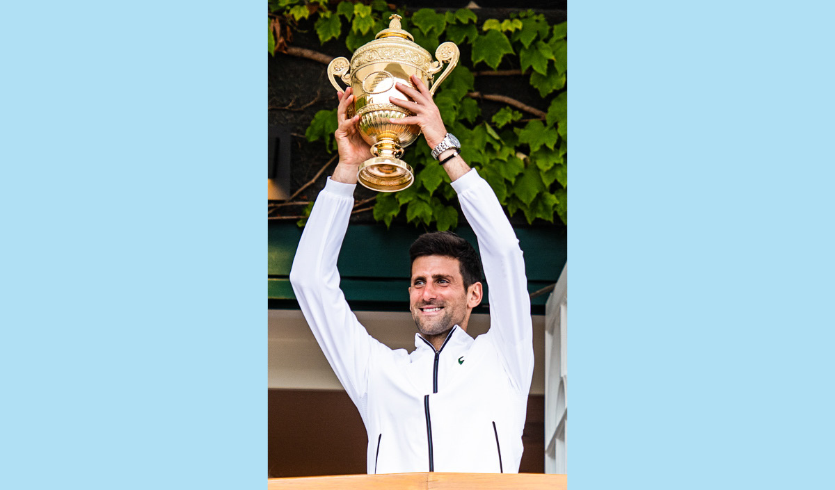 Photo of Novak Djokovi grinning and holding up a large trophy