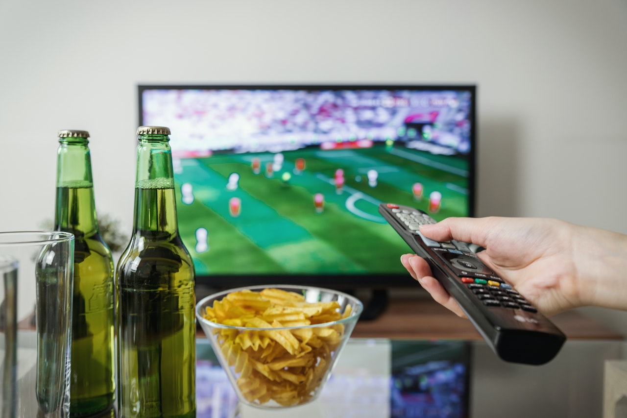 Photo of a person watching sports on TV with snacks and beer on the table in front of them.