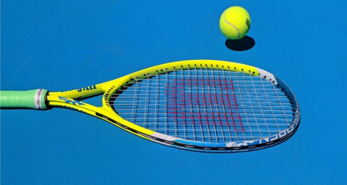 A tennis racket lying on the ground next to a tennis ball.