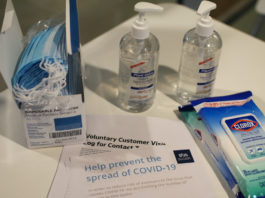 A table with hand sanitizer, disposable masks, clorox wipes, and a SUS handout on preventing the spread of COVID-19.