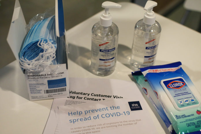 A table with hand sanitizer, disposable masks, clorox wipes, and a SUS handout on preventing the spread of COVID-19.