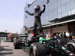 Lewis Hamilton standing on his F1 car, arms raised in celebration