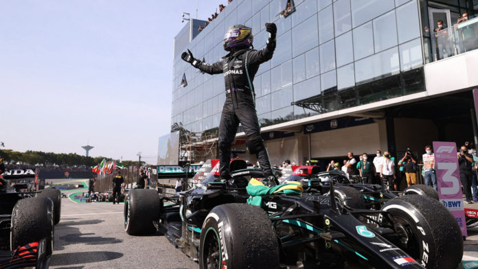 Lewis Hamilton standing on his F1 car, arms raised in celebration