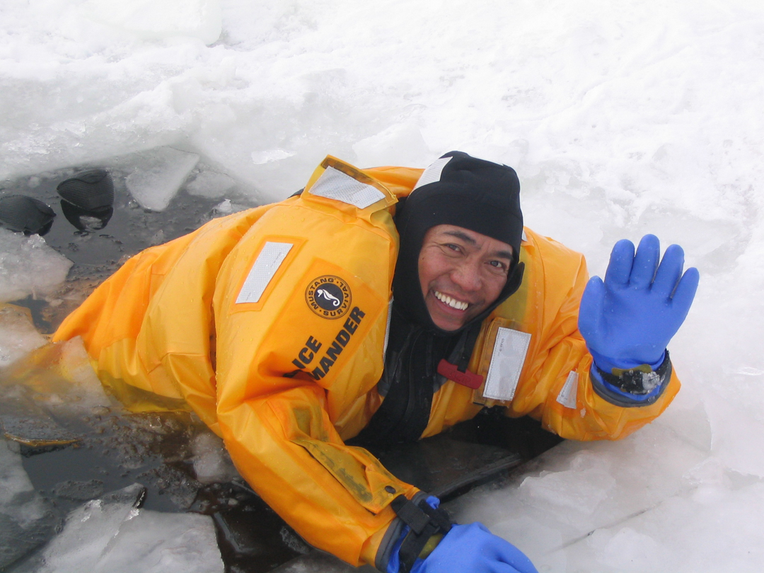 Photo of Dr. Mariano Mapili waving as he emerges from the a hole in icey water