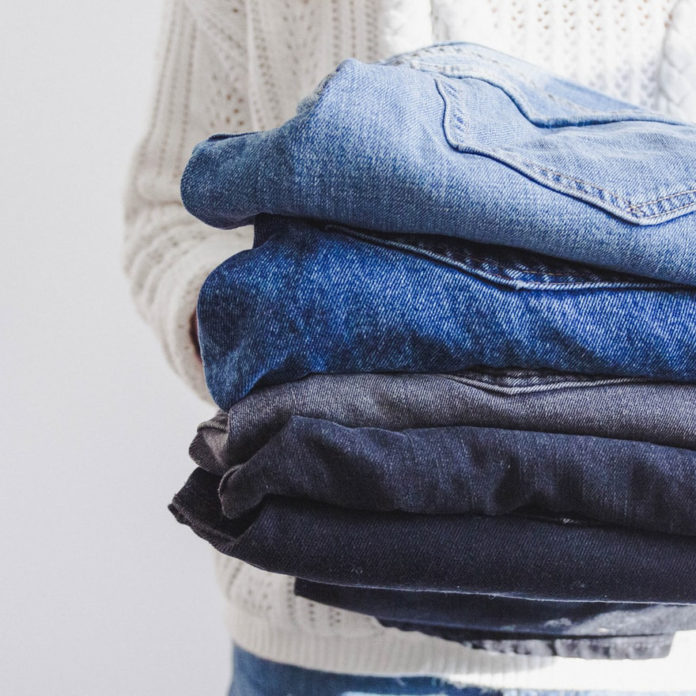 Photo of a person holding up a stack of jeans in different styles