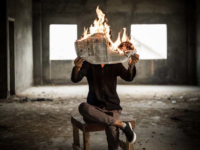 Photo of a person reading a newspaper while it burns