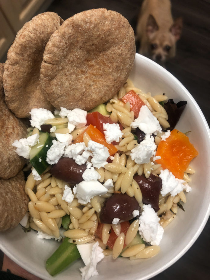 Photo of Greek Orzo Salad. A cute dog is out of focus in the background