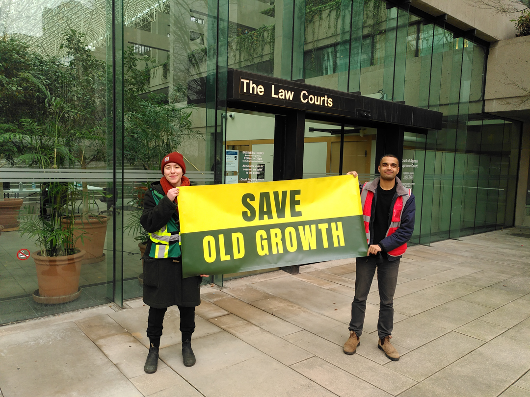 Photo of two people outside of BC Law Courts holding a banner that reads 