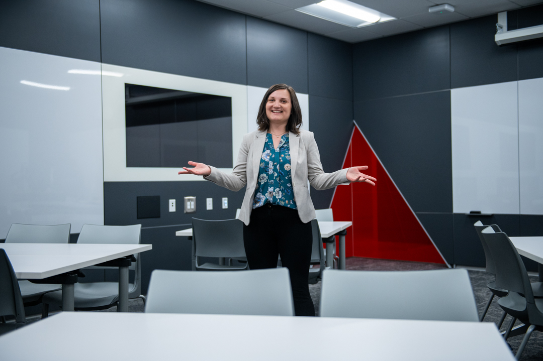 Photo of Dr. Judy Larsen in a modern-looking classroom, with arms wide and welcoming