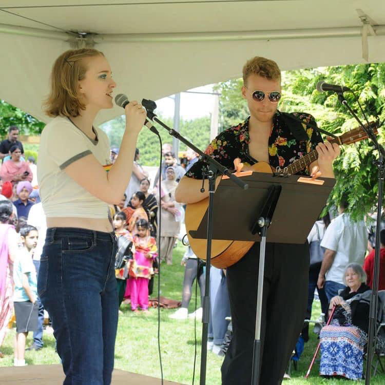 Photo of Olivia Keeping and Ryan Keeping playing music in a park for a watching crowd