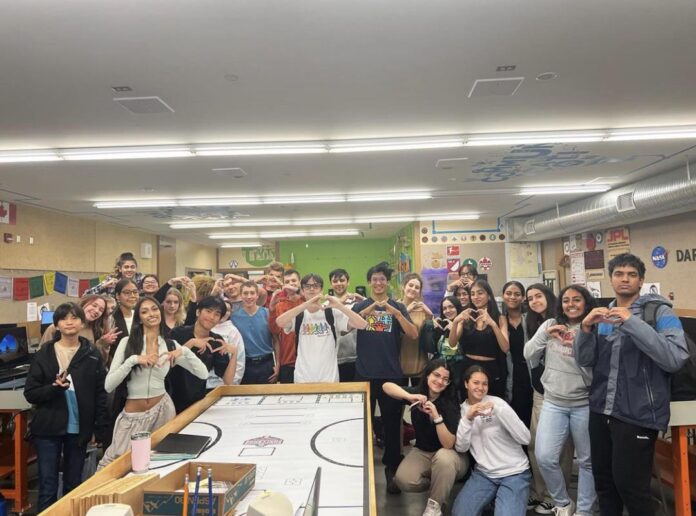 A group of High school students stand in a group. Some are making heart signs with thier hands.
