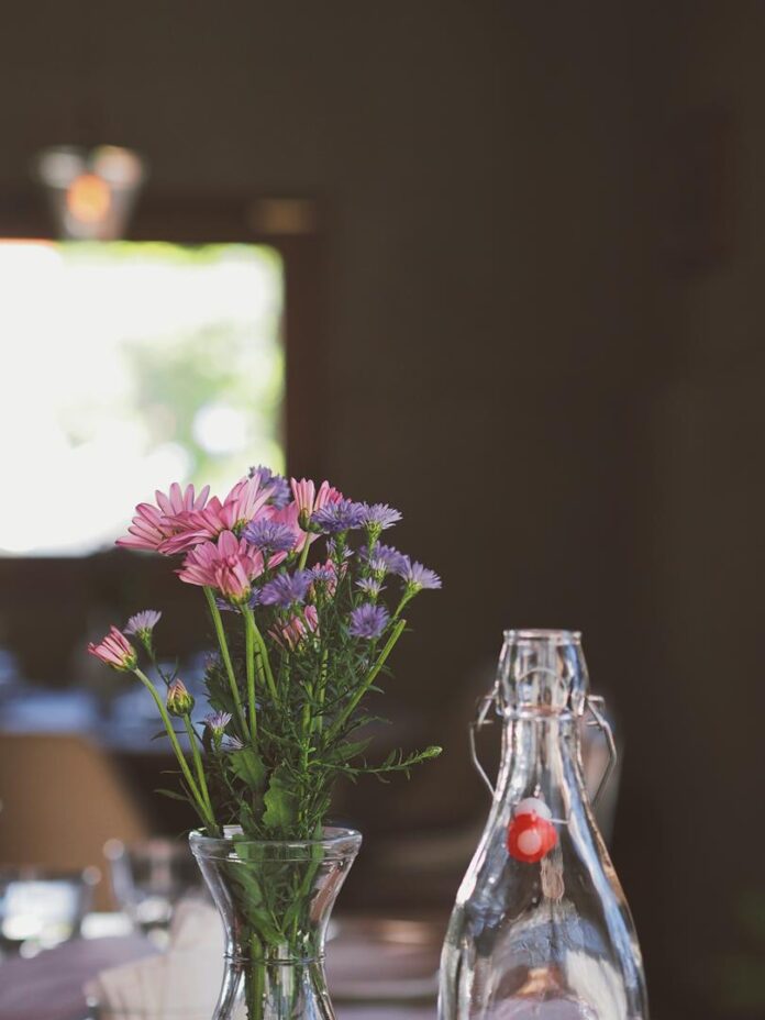 A bistro table with a bouquet of small purple and pink flowers in a vase and a clear glass bottle of water on top.