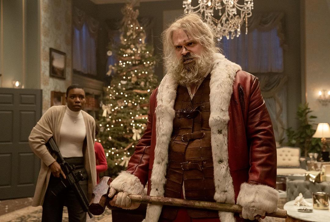 Santa standing in a room looking worn adn covered in blood. Behind him stands a character holding a gun.