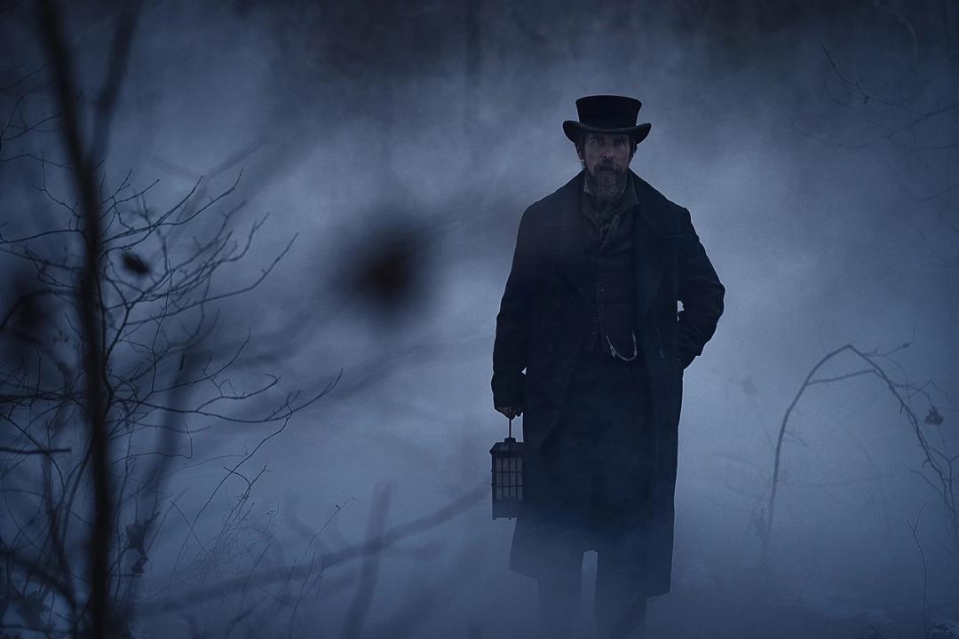 A male actor dressed in an old fashioned suit, walking through some dark misty woods