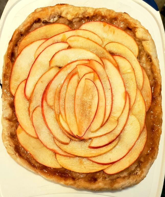 A white baking dish holds an apple tart with sliced apples artfully arranged on top.