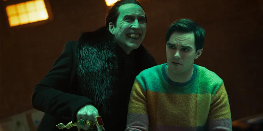 A scene from the movie where nicholas cage dressed as dracula is stading behind a younger man with his vampire teeth barred. There is a greenish tinge over casting the photo.