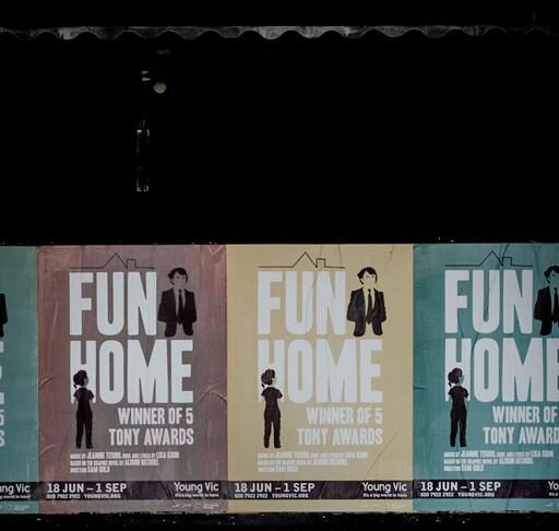 A woman in a baggy hoodie sitting under multiple signs saying "Fun Home"