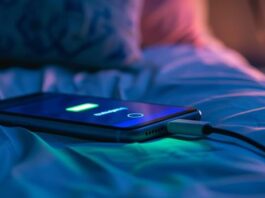 Close-up of a smartphone charging on a bed at night, creating a calm and cozy atmosphere. Generated AI